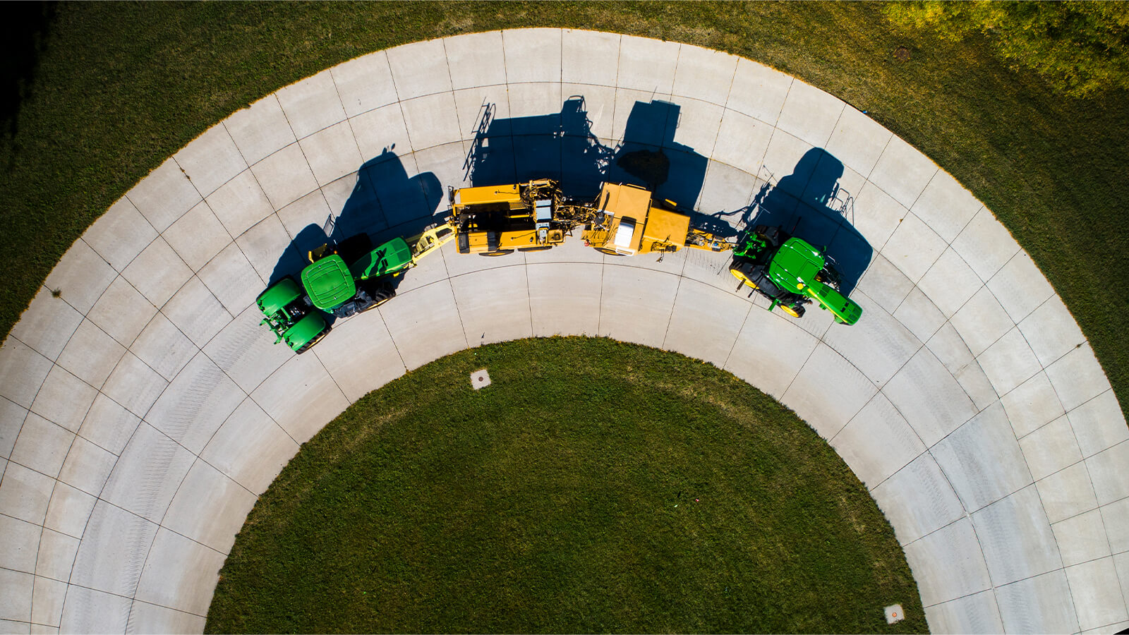 Three tractors in a line drive along cement circular track.