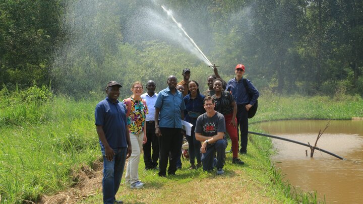 Group of students and faculty in front of a shoulder-high sprinkler near a pond in Uganda