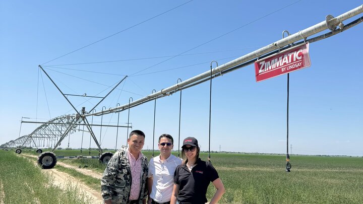 Three people standing in a field next to a Zimmatic center pivot irrigation system
