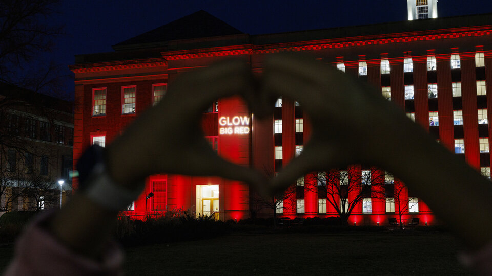 hands making the heart symbol in the background their is a building