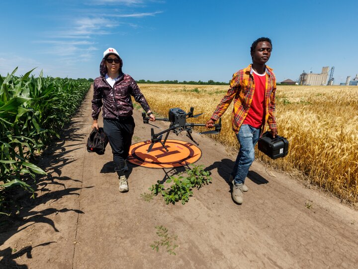 two students carrying  a drone in the middle of a field